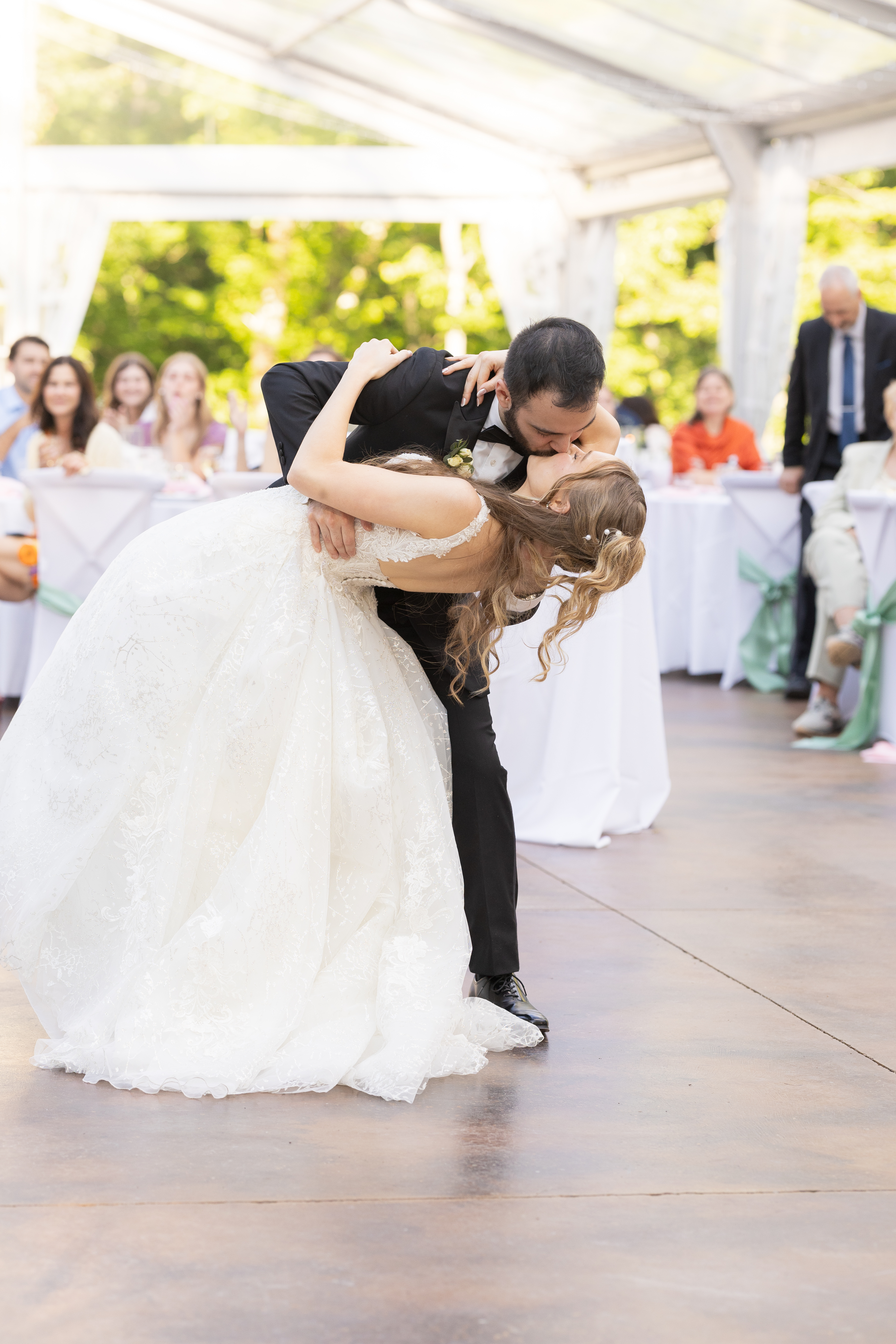 Groom dipping the bride backward into a kiss on the dance floor as guests look on