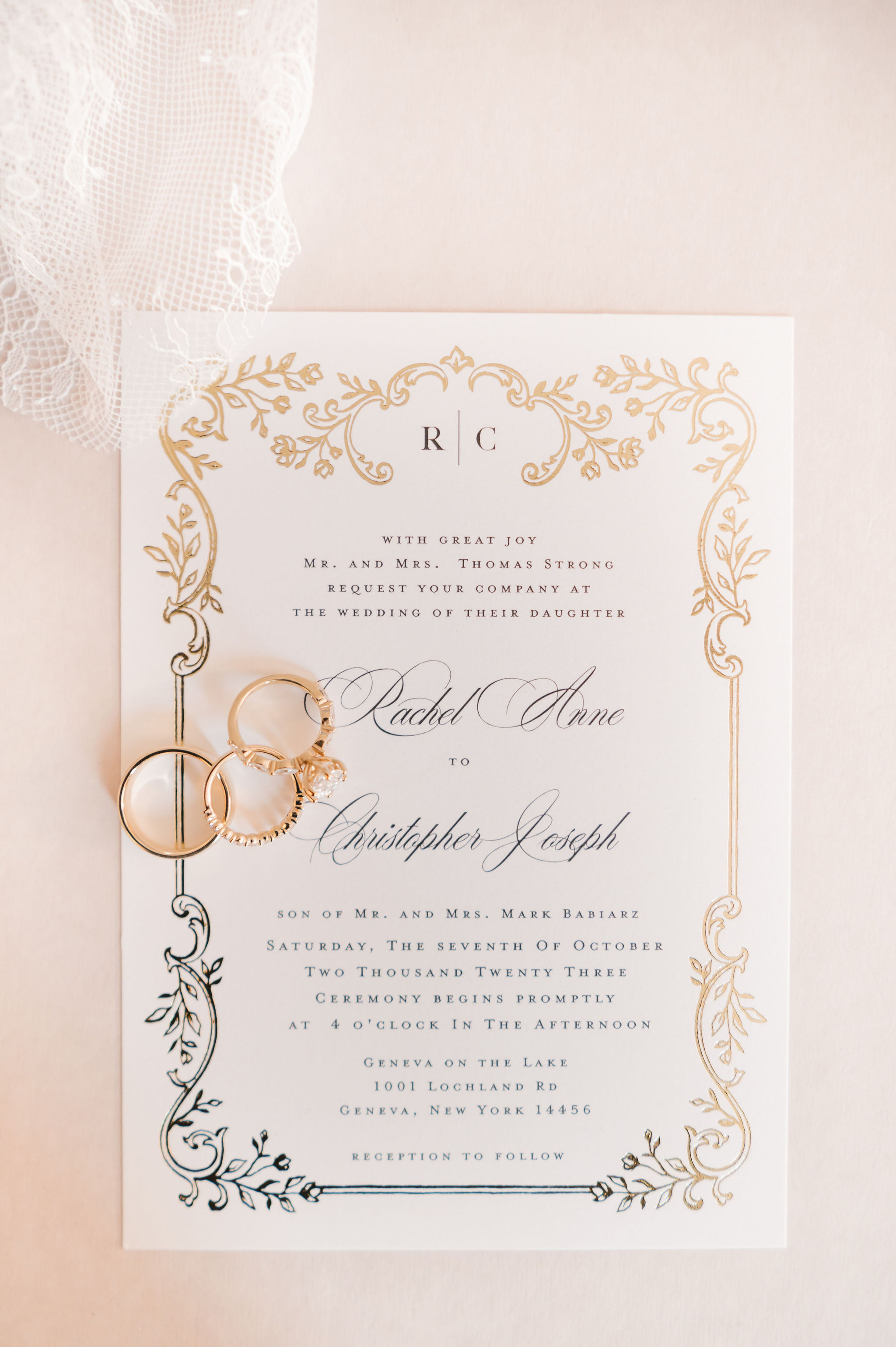 Ivory wedding invitation with an ornate gold foil botanical border and the monogram R and C, styled with gold rings and lace