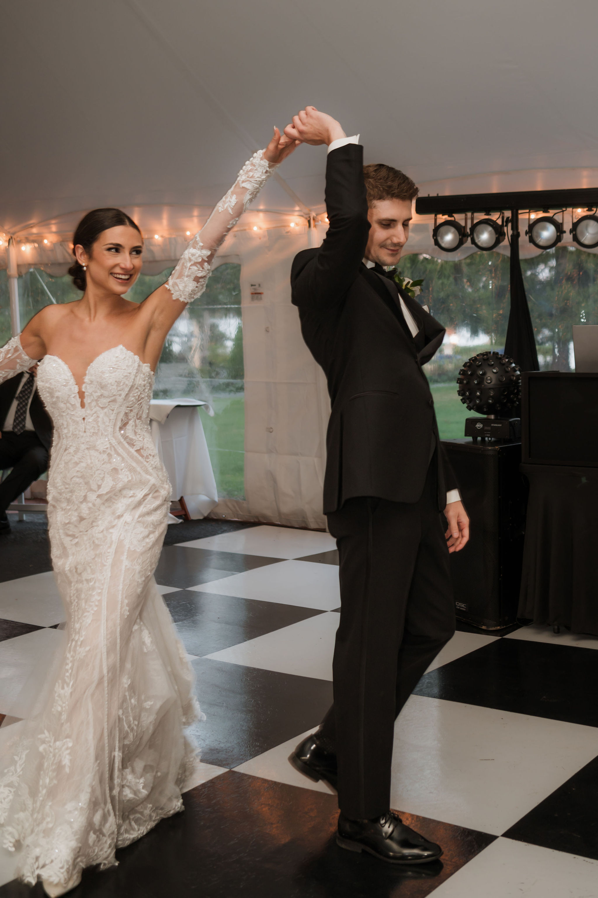 Groom turning the bride mid-twirl on a black-and-white checkered dance floor under a tent
