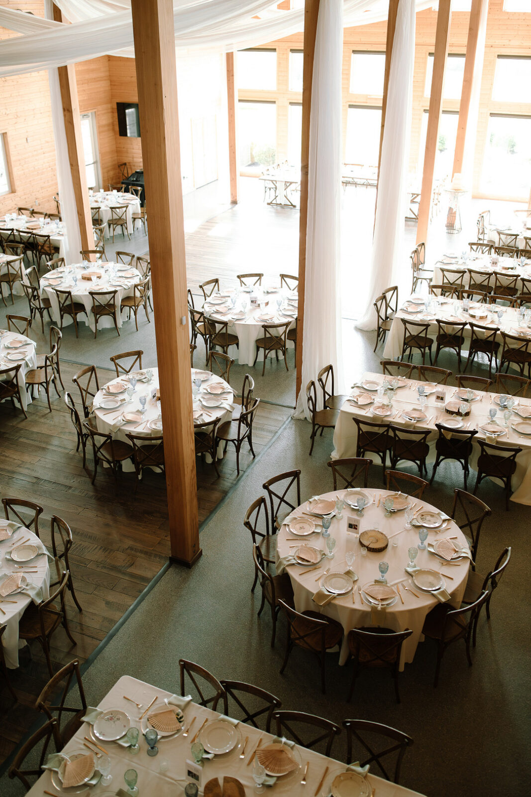 Large, bright event space at Stone Valley Meadows set with round and rectangular tables in white linens, each arranged with plates, glasses, and silverware—perfect for a formal Spring Woodland Wedding gathering.
