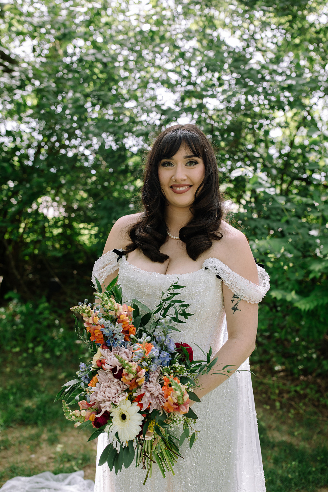 Bride with dark hair in loose waves and curtain bangs holding a colorful spring bouquet outdoors