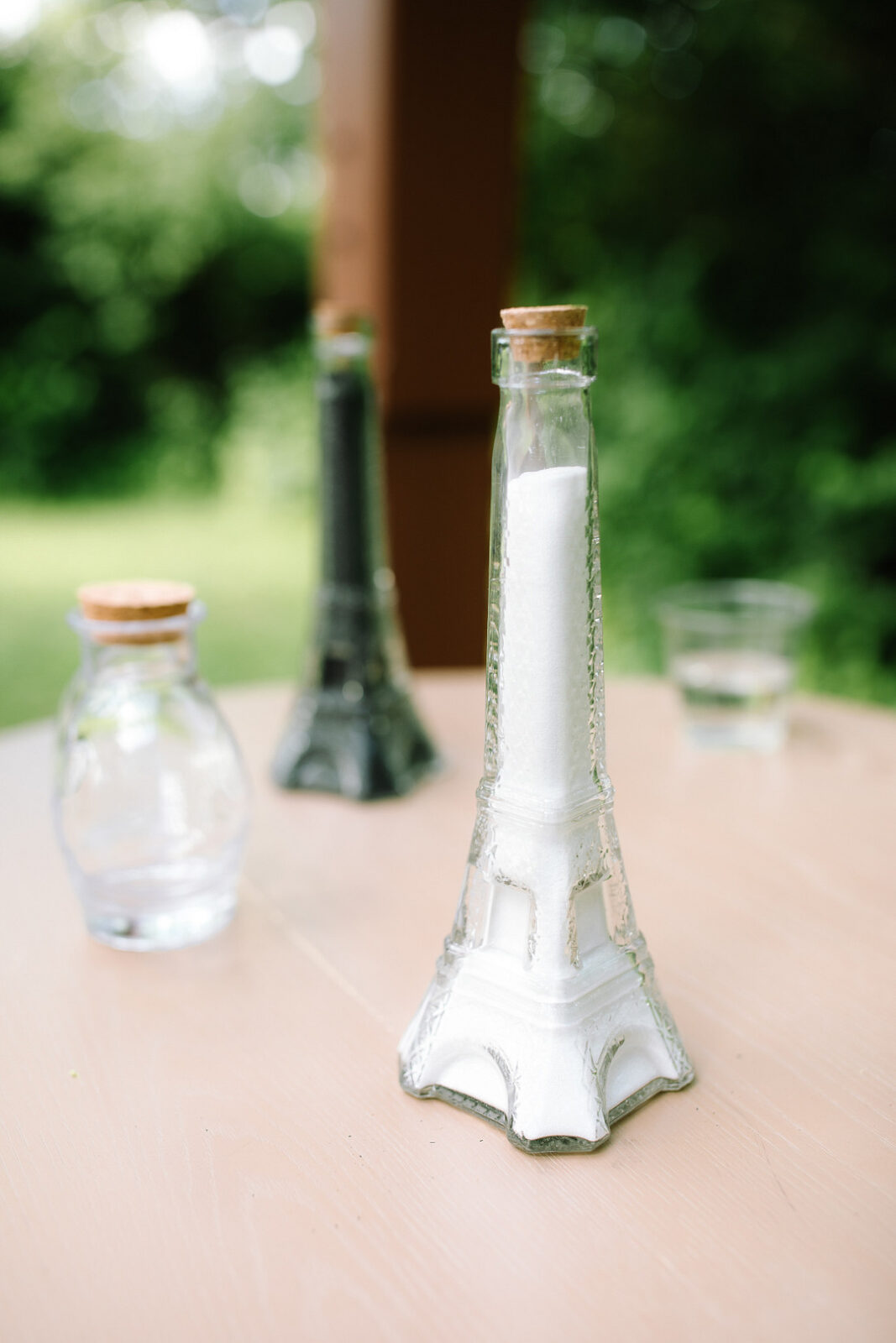A glass container shaped like the Eiffel Tower, perfect for a Spring Woodland Wedding at Stone Valley Meadows, is filled with white powder and sits next to a glass jar and another Eiffel Tower-shaped bottle containing a dark substance.
