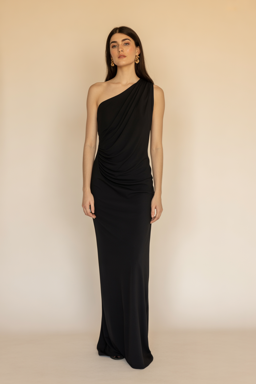 Woman standing against a plain background, wearing a black, one-shoulder, floor-length gown and gold earrings—a stunning choice for Black Tie Wedding Guest Dresses.