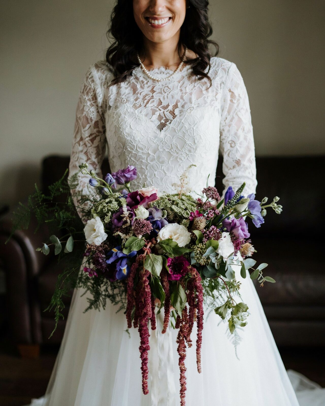 A woman in a white lace wedding dress holds a large bouquet of purple, white, and green fall wedding flowers—perfect inspiration for real weddings found on Pinterest.