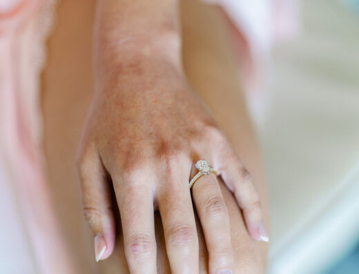 A close-up of a hand with pale pink manicured nails resting on a knee, wearing a diamond engagement ring—perfect for an elegant wedding at Cielo Farms.
