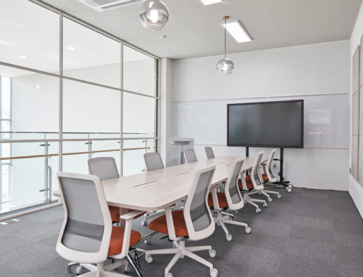 Modern conference room with a long table, ten office chairs, a large screen, glass walls, and pendant lights. The room is clean, bright, and minimalistic.