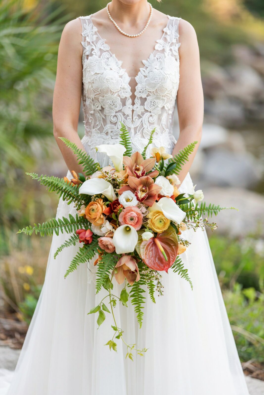 A bride in a lace wedding dress holds a large bouquet of assorted flowers and ferns, perfect inspiration for real weddings and those seeking fall wedding flowers on Pinterest.