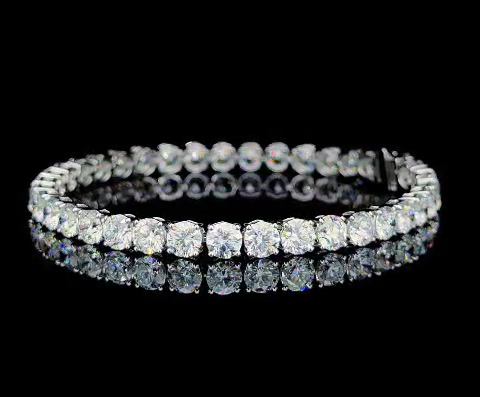 A diamond tennis bracelet with round-cut stones set in a single row, displayed on a reflective black surface.