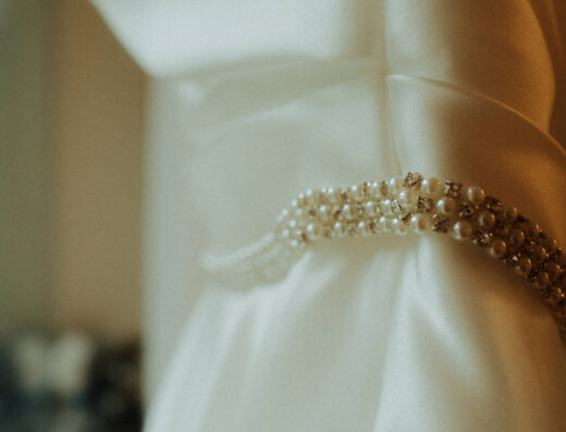 Close-up of a white satin garment with a beaded pearl belt wrapped around the waist, softly lit with a blurred background.