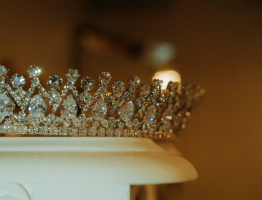 A close-up of a sparkling diamond tiara resting on a white surface with a blurred brown background.