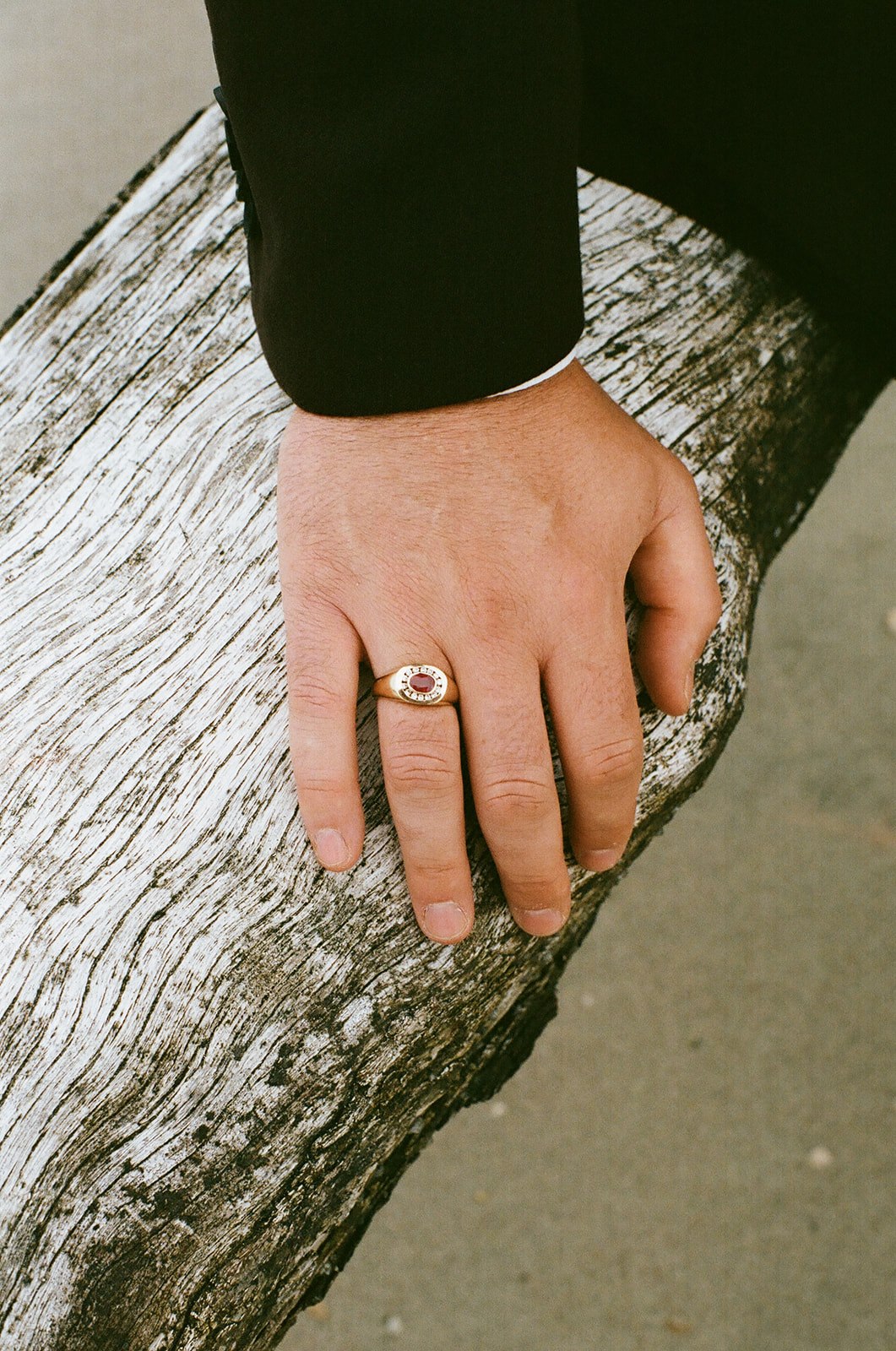 A person wearing a black sleeve rests their hand with a gold ring on a weathered, whitewashed log.