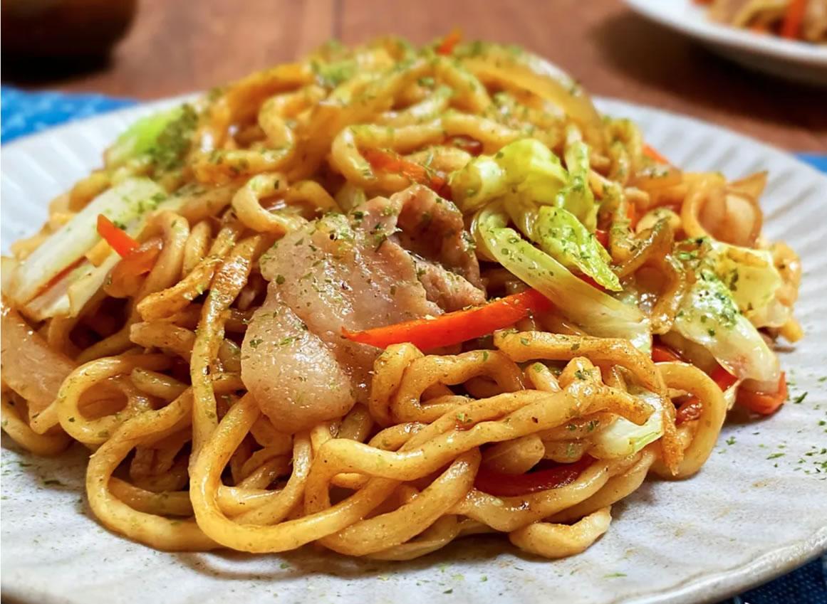 A plate of yakisoba noodles with sliced pork, cabbage, and carrots, garnished with green herbs—perfect for a hibachi dinner or as a flavorful addition to your Hibachi wedding reception entertainment.