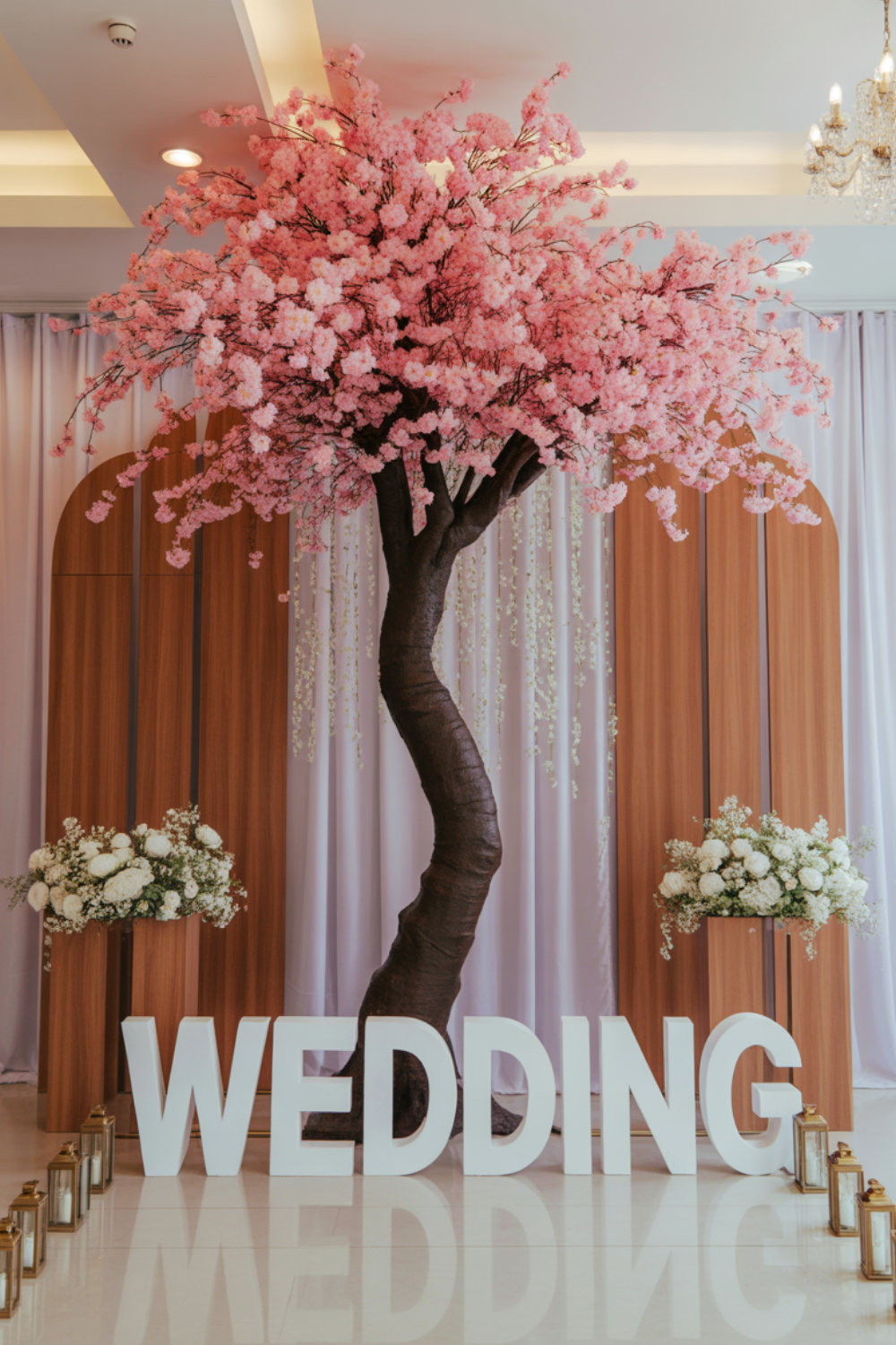 Pink artificial cherry blossom tree set against curved wooden arch panels and pale drapes, with white floral clusters on the panels and lanterns along the floor