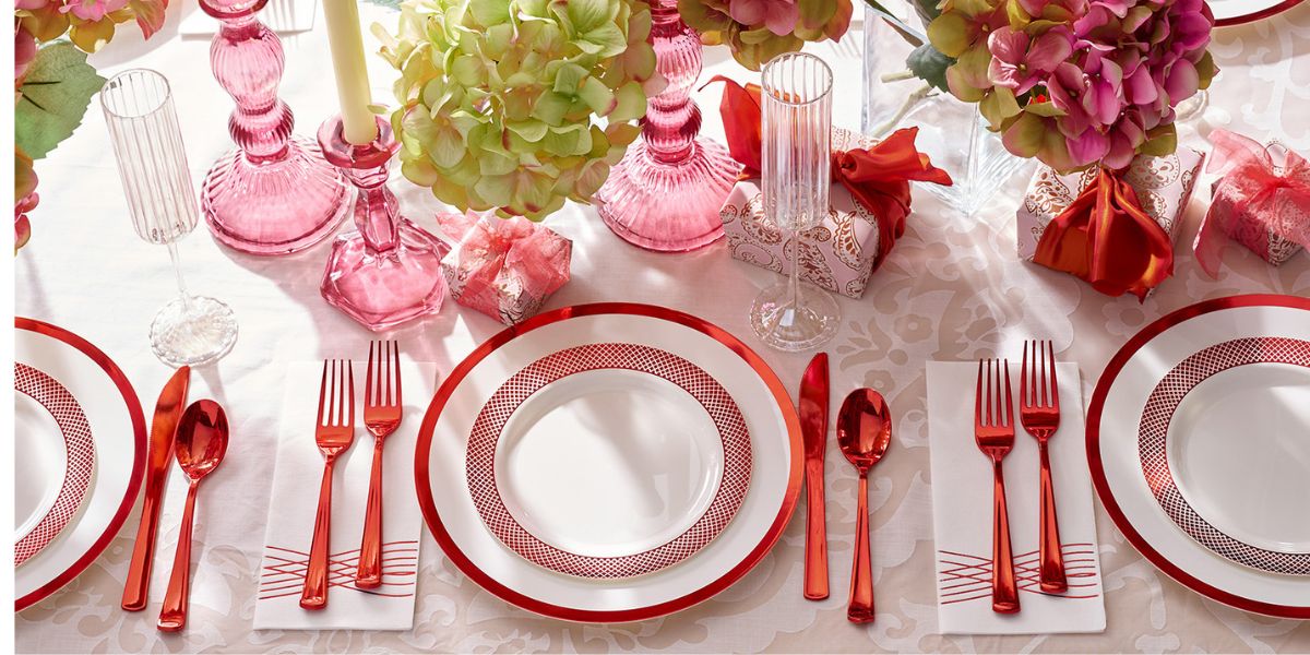 A formal table setting with elegant disposable red utensils, white plates with red borders, pink glassware, and floral centerpieces on a white tablecloth—perfect for sophisticated wedding table settings.
