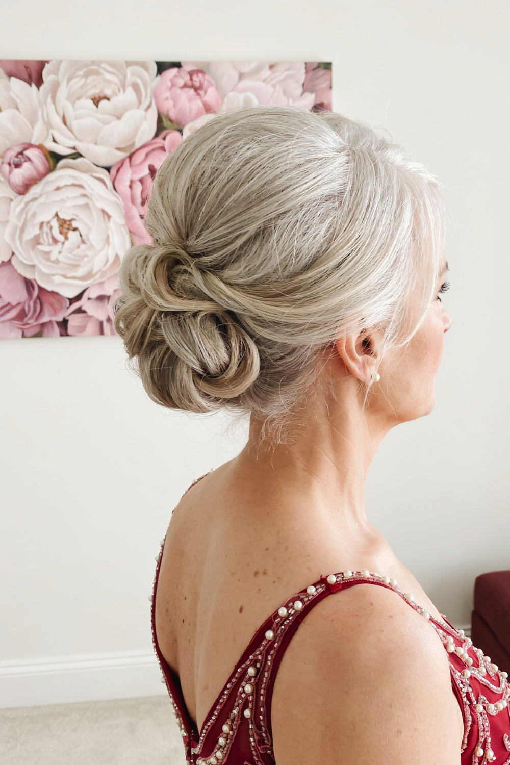 Silver blonde twisted low bun worn with a deep red beaded gown, side back view