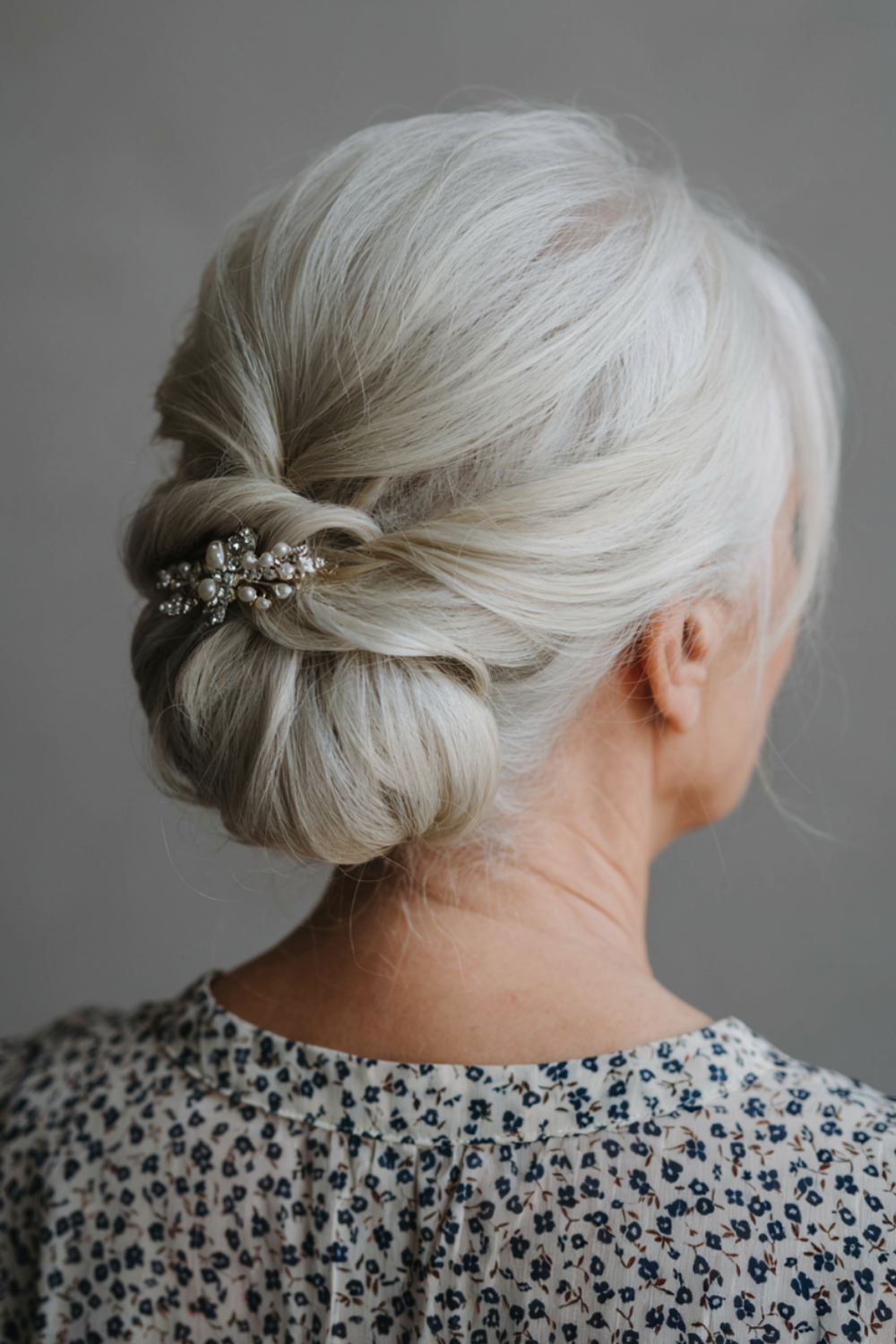 White hair in a low rolled chignon with a pearl and crystal comb and soft face-framing pieces, back view