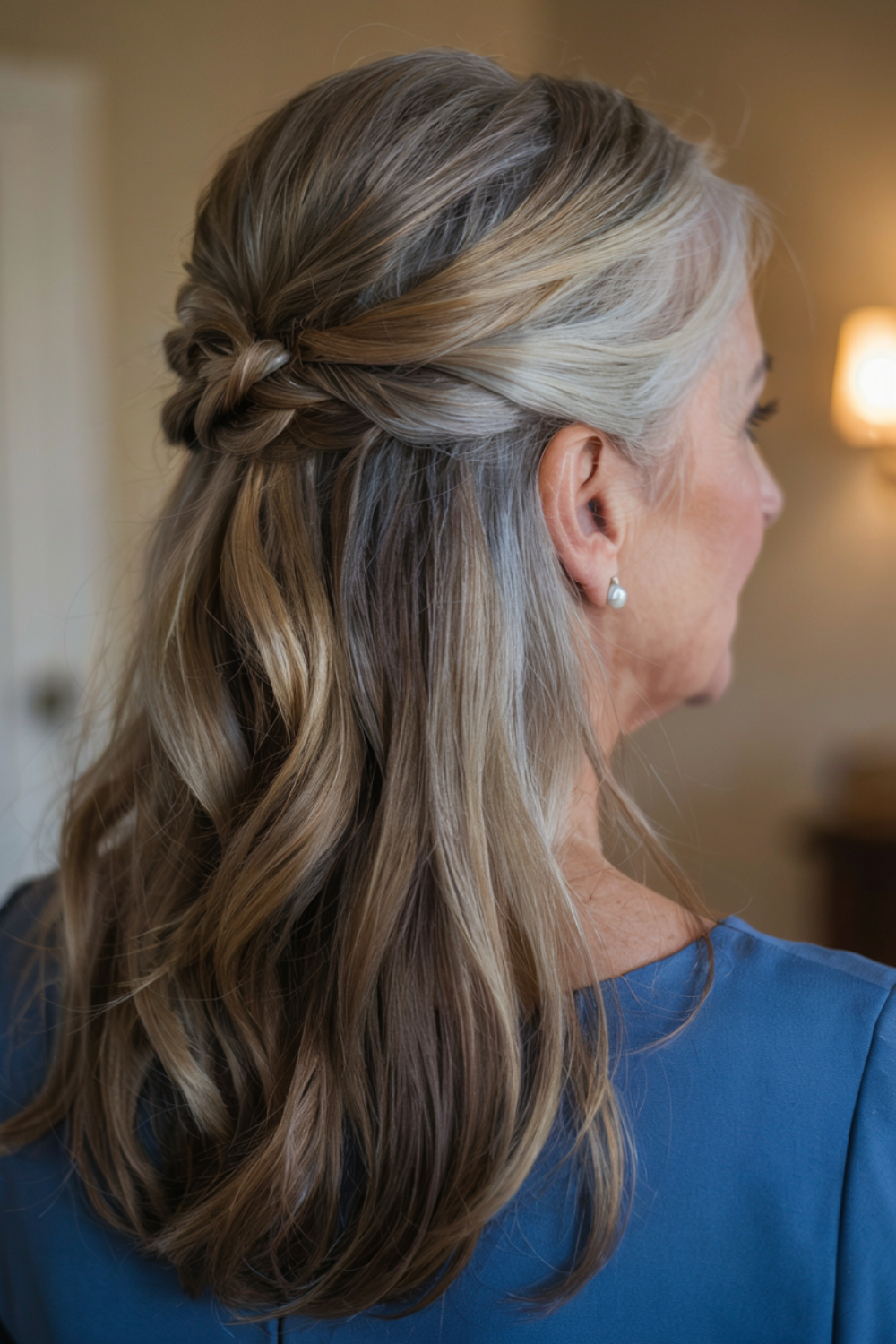 Half-up hairstyle with a twisted knot at the back, blonde and grey blended long hair left loose underneath