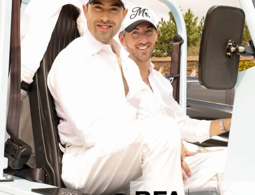 Two men, Eric Viner and Jordan Wise, dressed in white and wearing “Mr.” hats, sit smiling in an open vehicle. They appear relaxed and happy, capturing a joyful moment from their Hamptons wedding.