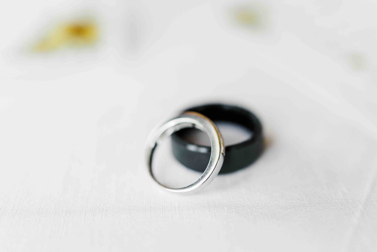 A silver ring and a black ring rest on a white surface, with the silver ring resting inside the black ring.