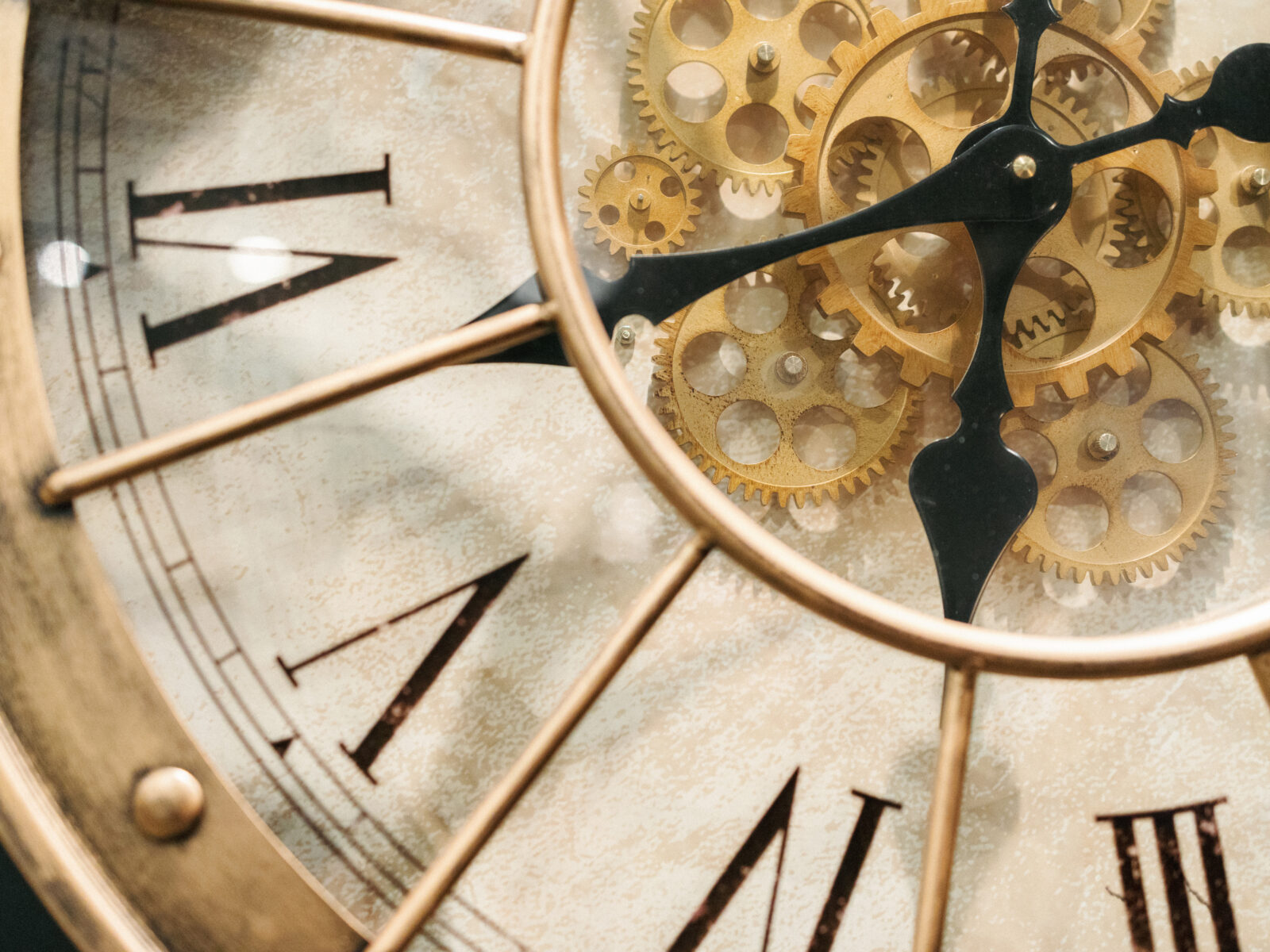 Close-up of a vintage clock face with Roman numerals and visible gold gears behind the clock hands.