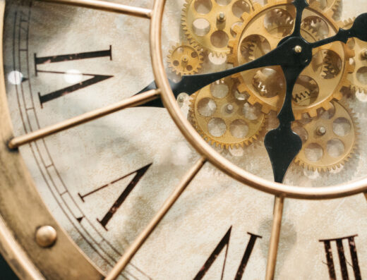 Close-up of a vintage clock face with Roman numerals and visible gold gears behind the clock hands.