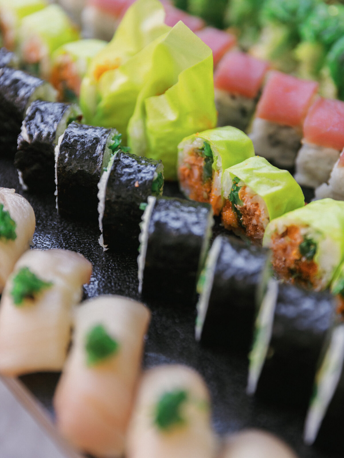 Assorted sushi rolls, including nori-wrapped and yellow soy paper rolls, arranged neatly on a black platter.