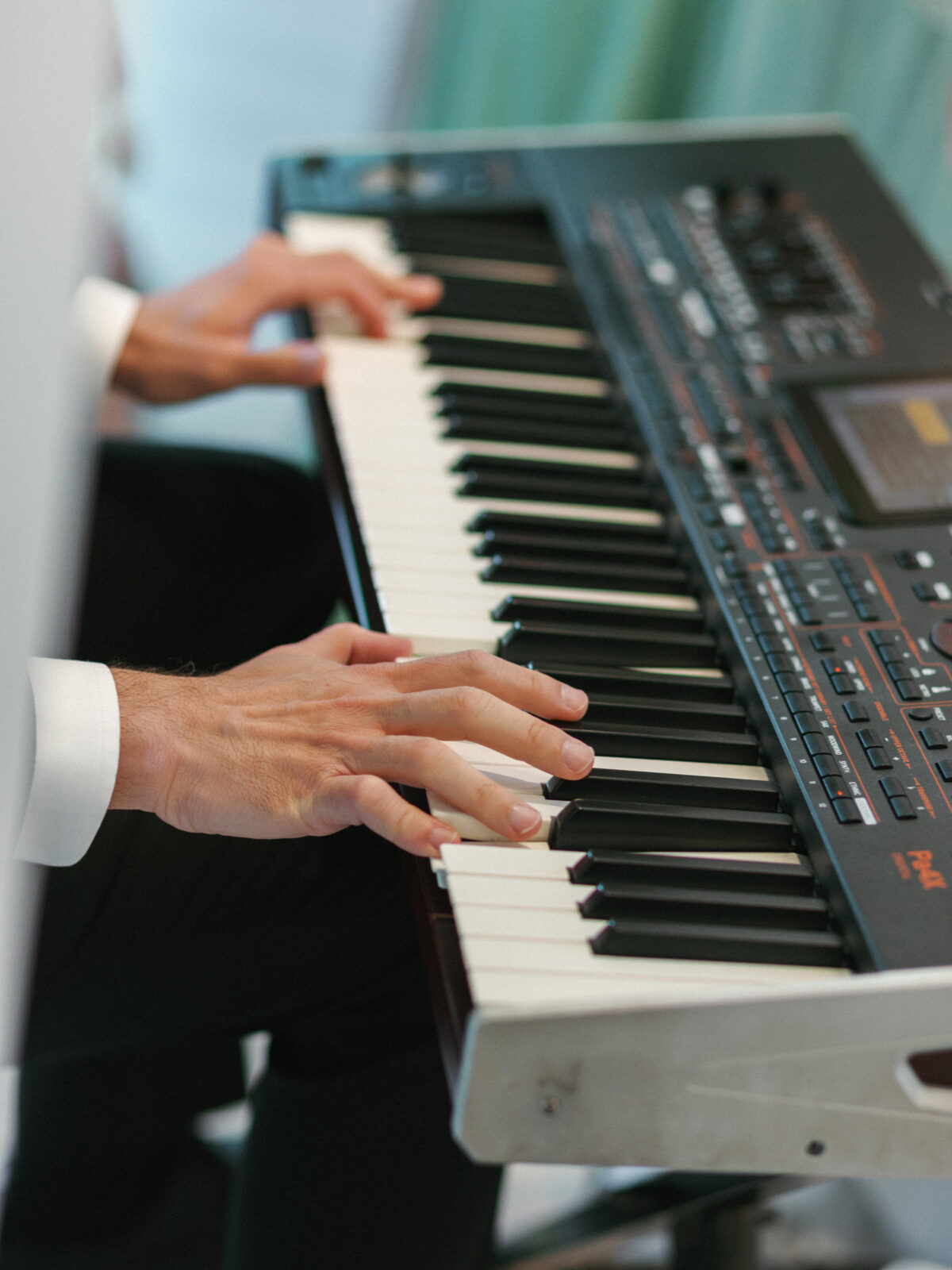 A person in a white shirt plays a black electronic keyboard with both hands, focusing on the keys.