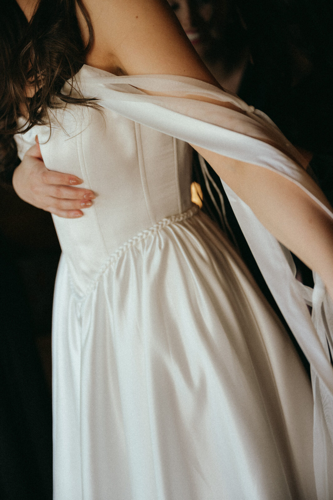 A person wearing a white, strapless dress with draped fabric over their shoulders and another hand gently touching their waist.