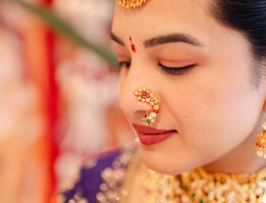 A woman wearing traditional gold jewelry, including a maang tikka and a nose ring, with a red bindi on her forehead.