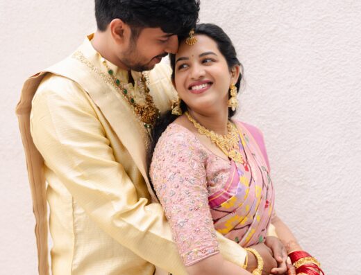 A bride and groom in traditional Indian wedding attire embrace while looking at each other.